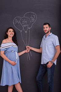 儿童的想象力摄影照片_怀孕的夫妇在粉笔板上画出他们的想象力
