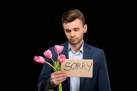 心烦意乱的年轻人拿着粉色郁金香花束和黑色的抱歉标志