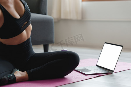 年轻女子在家练习瑜伽，跟随老师在笔记本电脑在线课堂上练习。