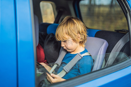小男孩在汽车后座上使用触摸板在旅途中自娱自乐