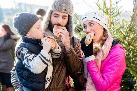 家庭在圣诞市场上吃面包卷和香肠