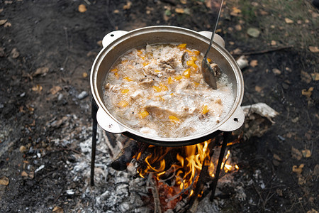 在户外休闲时，一口装有由鸡翅和蔬菜制成的沸腾鸡肉浓汤的大锅放在火上。