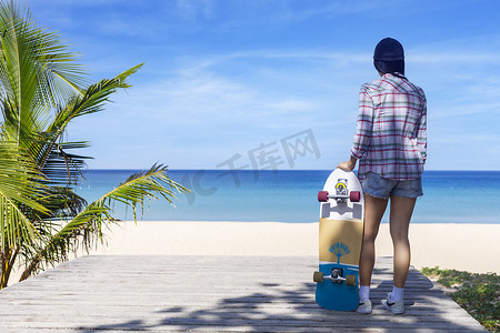 极限冲浪摄影照片_年轻女性拿着海滩背景的冲浪滑板。
