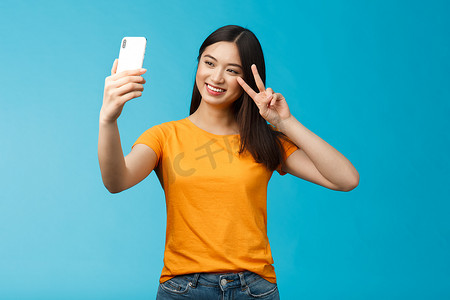 友好开朗漂亮的亚洲女性黑发短发自拍，快乐地微笑着拿着智能手机展示和平，在手机屏幕前置摄像头上的胜利标志，谈论家庭视频通话