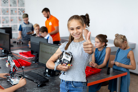 一个快乐的女学生在机器人课上的肖像，她拿着一个机器人，它是由在计算机上编程的塑料部件组装而成的。