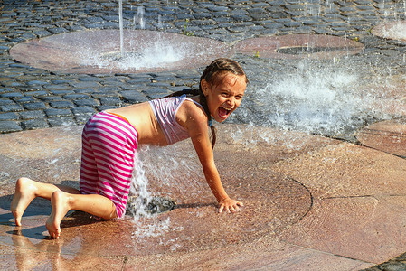 明媚春天摄影照片_在阳光明媚温暖的日子里，女孩在外面的喷泉里玩耍。