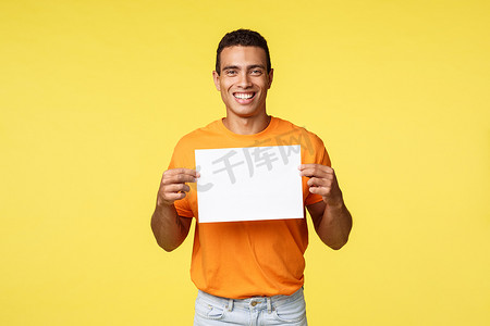 穿着橙色 T 恤、笑得开心的西班牙裔男性，把纸放在胸前，咧嘴笑着给出建议，写下最喜欢的产品或商店网站，给出建议，推荐购物点，黄色背景