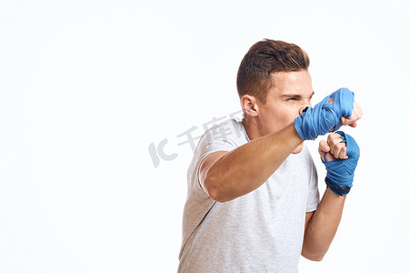 戴着蓝色手套的运动型男拳击手在浅色背景裁剪视图中练习拳击