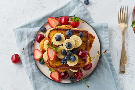 切片水果摄影照片_法式烤面包配浆果和香蕉、奶油蛋卷早餐、白色背景、顶视图