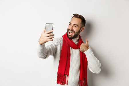 留着胡子的快乐男人视频通话，在手机上竖起大拇指，比如圣诞礼物，在线聊天，站在白色背景上