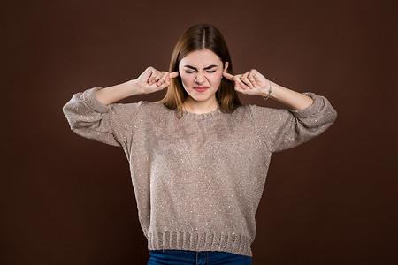 关闭肖像愤怒压力大的年轻女子用手指堵住耳朵，被吵闹的噪音激怒，头痛或偏头痛。