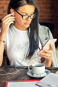 戴眼镜的漂亮女人正在咖啡馆用智能手机听音乐。