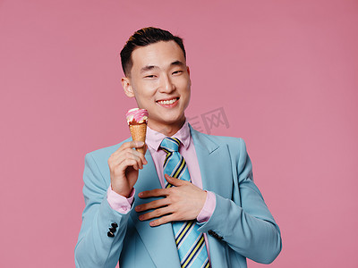 快乐的亚洲人，拿着冰淇淋蓝色西装，欢快的粉红色背景
