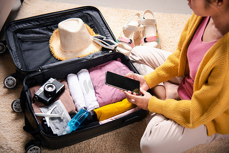 广交会箱包海报摄影照片_使用智能手机空白屏幕和包装手提箱包在家旅行周末度假的女性