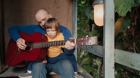 弹吉他的小孩摄影照片_爸爸为他的小孩弹一把原声吉他。