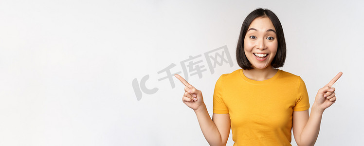 手指左右摄影照片_可爱的亚洲女孩侧指手指，展示左右促销，两种选择，产品变体，站在白色背景的黄色 T 恤上