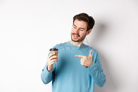 帅气的白人男子用手指着咖啡杯，推荐咖啡馆，站在白色背景上满意