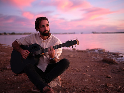 黄昏时分，坐在粉红湖岸边的石头上弹吉他的男人