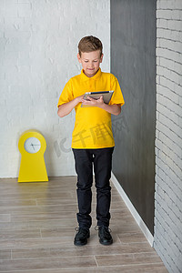 穿着黄色T恤领带和时尚靴子的可爱帅气的男学生站在靠近黑板的地方，上面有数字，拿着平板电脑，微笑着
