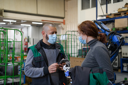 智能数控摄影照片_戴着面罩防止日冕病毒的工业工人讨论工厂生产。