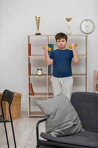 一个小男孩在他的房间里用哑铃锻炼。