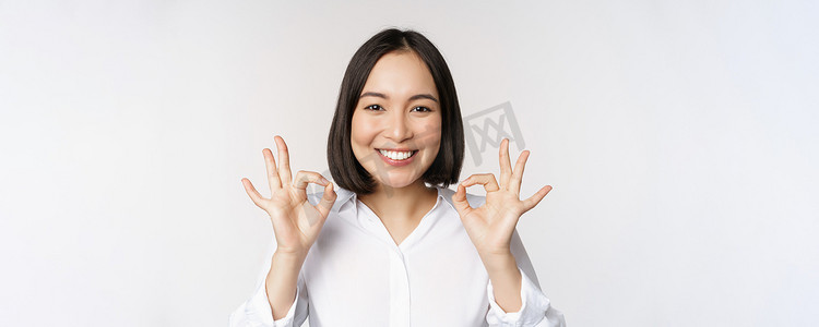 特写亚洲女孩的头像，表现出好的、好的手势和满意的微笑、推荐、高兴、赞美和恭维，白色背景