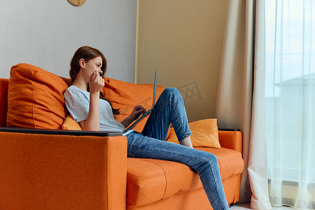 橙色客厅摄影照片_欢快的女人在橙色沙发上用笔记本电脑技术聊天