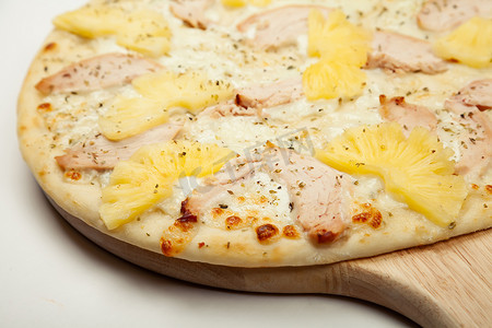 凤梨肉摄影照片_质地美味的夏威夷披萨放在木盘上，配料为大蒜酱、马苏里拉奶酪、熏鸡、白色罐装菠萝。