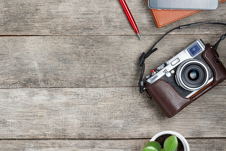 灰色木质背景上的经典相机，配有棕色记事本、红笔、电话和绿色植物。