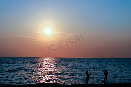 剪影两个人站着在海滩日落拍照