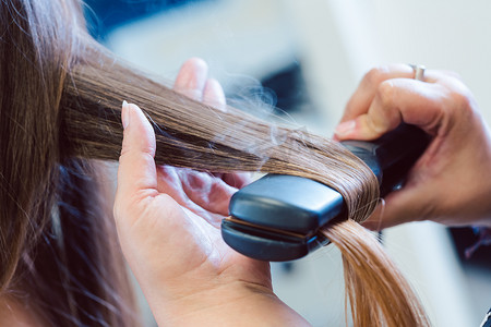 美发师在女性顾客的头发上使用扁铁