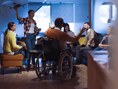 坐在轮椅上的残疾商人在现代开放空间联合办公室工作，团队使用虚拟现实谷歌无人机辅助模拟