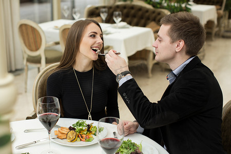 互相喂食摄影照片_美丽的年轻夫妇在餐厅度过时光时互相喂食和微笑。