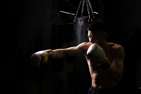 医用pvc手套摄影照片_练习拳击运动员的拳击袋手套黑色年轻背景身体，从肌肉发达的拳击手套中适合竞争、训练侵略。
