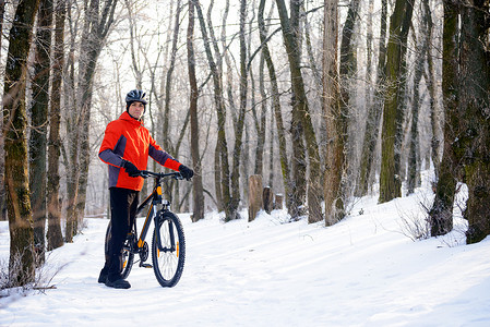骑自行的男孩摄影照片_美丽的冬季森林雪道上骑自行车的山地自行车手