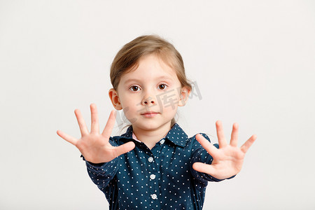 4-6 岁的白人小女孩穿着一件带圆点的蓝色连衣裙，将手掌伸向镜头