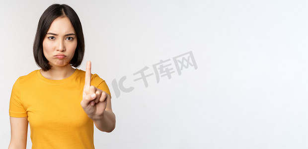 禁止手势摄影照片_亚洲女性的肖像看起来严肃而愤怒，展示停止禁止手势、禁忌标志、禁止 smth，站在白色背景上的黄色 T 恤