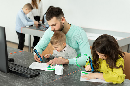 年轻的父亲和他的儿子和女儿在机器人课上用 3D 笔画了一幅画。
