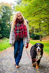 行走的女人摄影照片_在公园里用皮带遛狗的女人