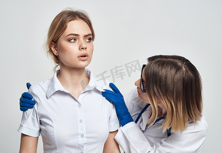 一位戴蓝色手套的护士在浅色背景中检查一位身穿白色 T 恤的病人