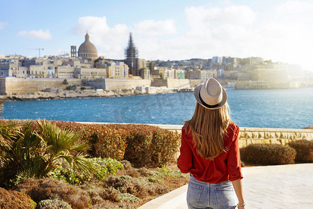 戴着帽子的迷人女人沿着马耳他海滨走下去，看着马耳他瓦莱塔美丽的城市景观