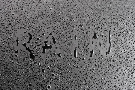下雨图片摄影照片_带水滴的哑光黑色疏水哑光表面上手写的“雨”字