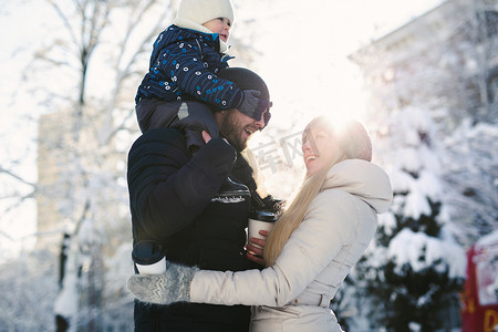 一个快乐的年轻家庭在冬季城市公园里一起散步的肖像，阳光下。