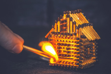 手拿着燃烧的火柴点燃火柴、风险、财产保险保护或可燃材料概念点火的房屋模型