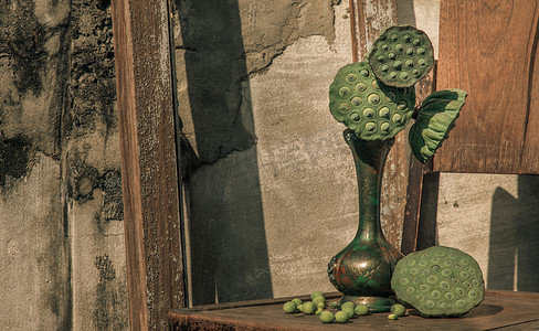 花瓶古董摄影照片_古董雕刻铁壶或旧木椅上的花瓶中的新鲜绿色莲子荚。