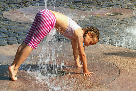 在阳光明媚温暖的日子里，女孩在外面的喷泉里玩耍。