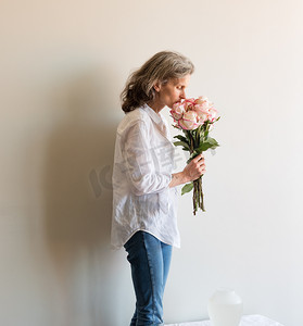 桌上花瓶附近，头发花白，白衬衫闻着粉红色和奶油色玫瑰的中年妇女
