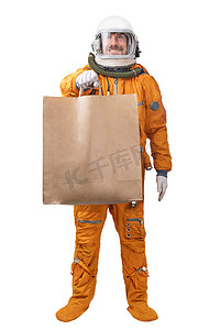 快乐的宇航员身穿橙色太空服和太空头盔，手拿空白牛皮纸袋，背景为白色。