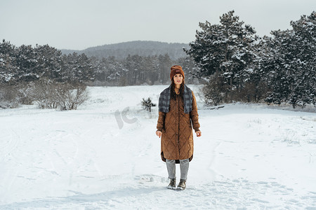 下雪保暖摄影照片_穿着冬季保暖夹克的女人在多雪的冬季森林里行走