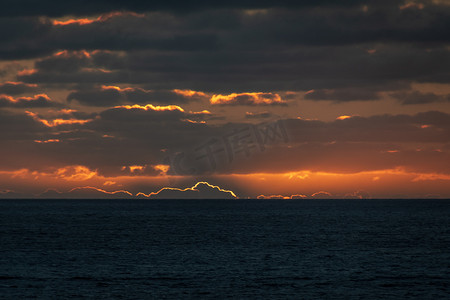 云朵橙色摄影照片_太阳已经落到地平线后面，给云朵呈现出橙色的轮廓